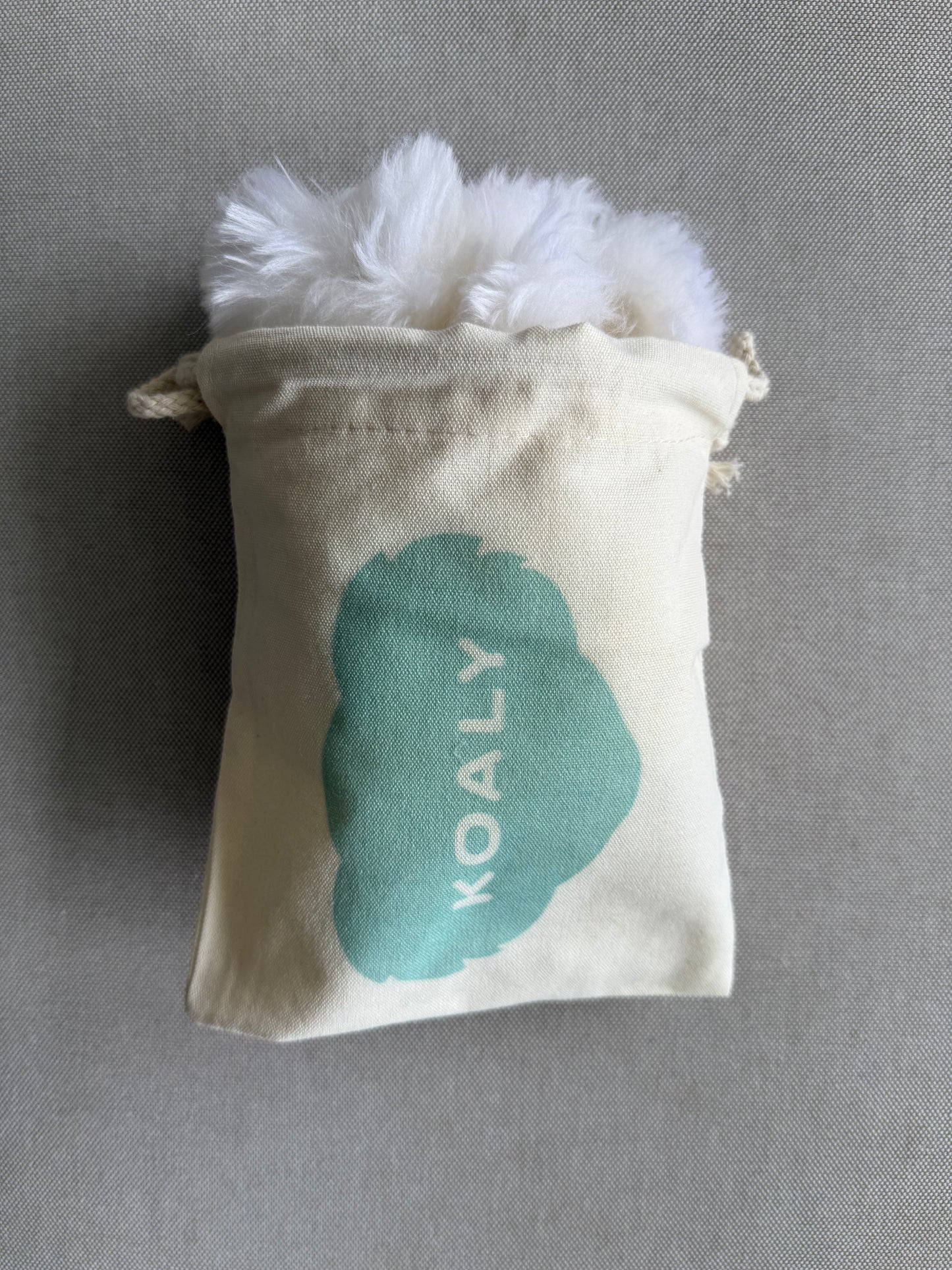 Small pouch with fluffy white sheepskins strap covers and 'KOALY' branding on a gray background
