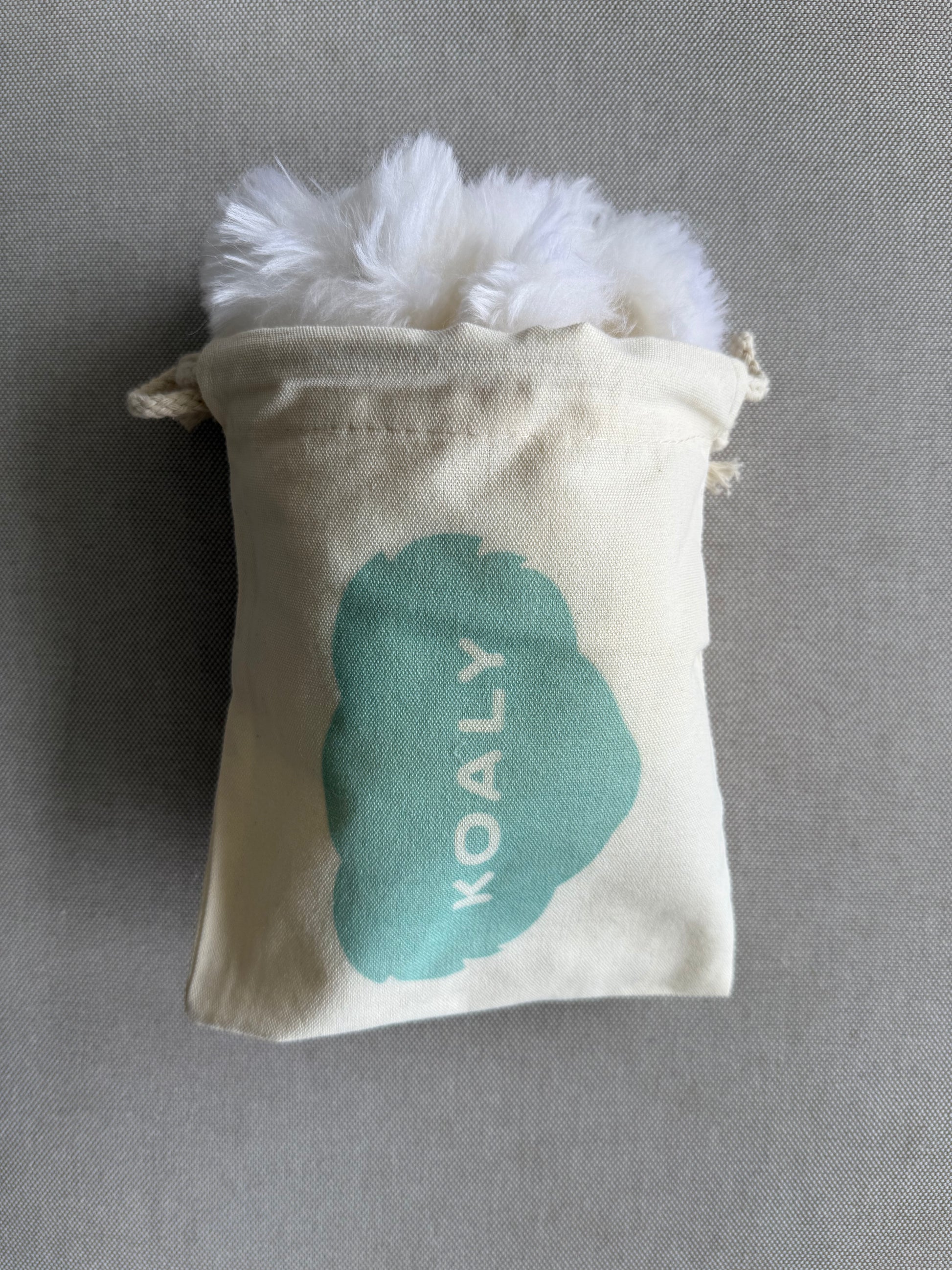 Small pouch with fluffy white sheepskins strap covers and 'KOALY' branding on a gray background
